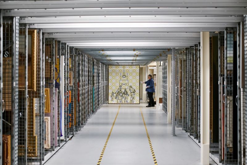 Geelong Gallery Collection Storage, rows of paintings hun in wire racks down a long hallway with a person at the end