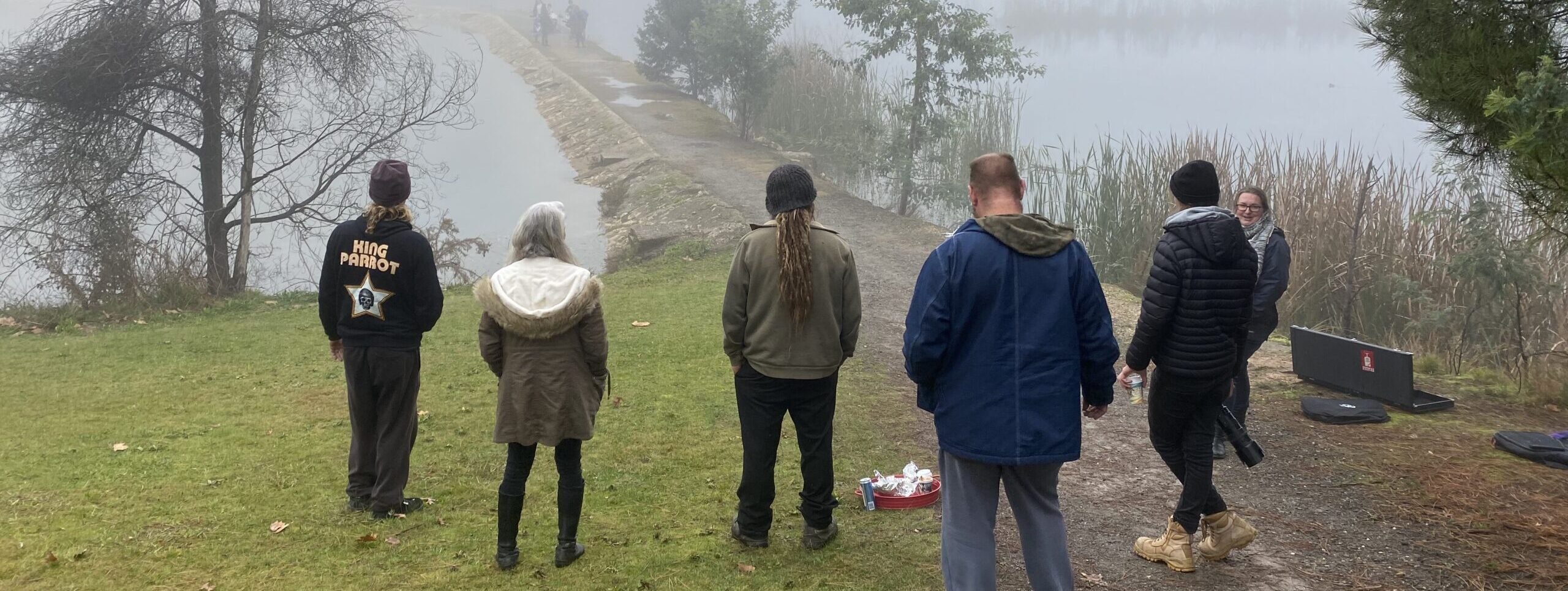 a number of people stand beside a lake with mist
