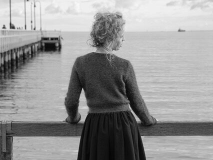Black and white photograph of a woman standing next to a pair looking out over the water