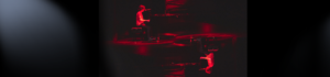 A young man sitting at a piano on a stage washed with dark red lighting